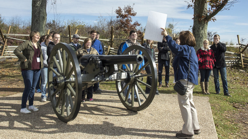 Students at Gettysburg listening to tour guide next to a cannon.
